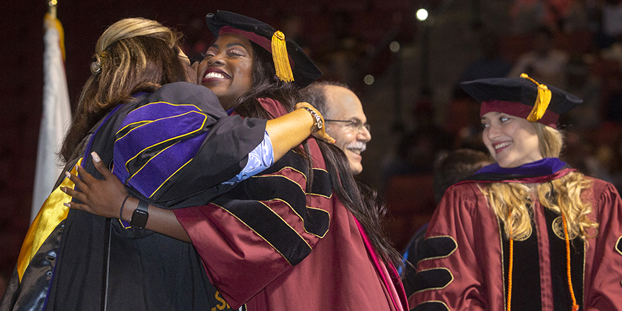 Graduate hugging faculty member on stage